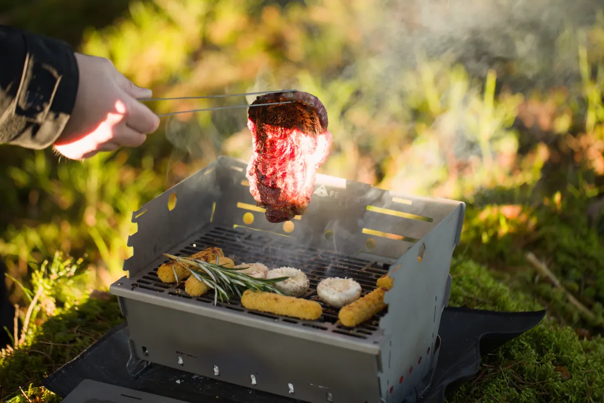 Titanium tongs lifting a steak from the Titan1 grate