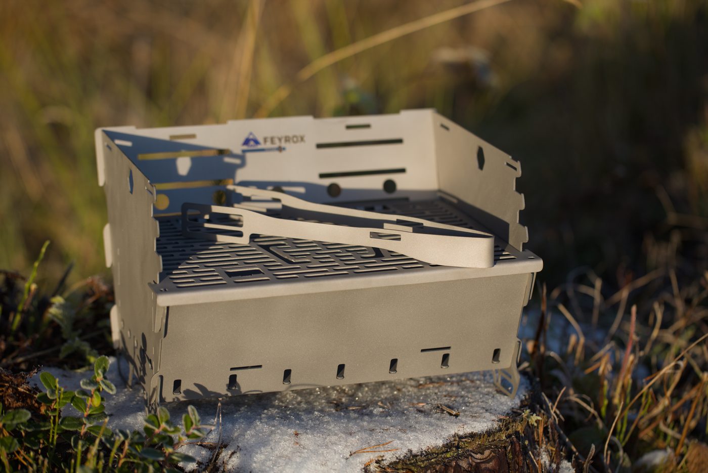 Titan1 assembled with the grate, tongs and skewers resting on top, set on a rock