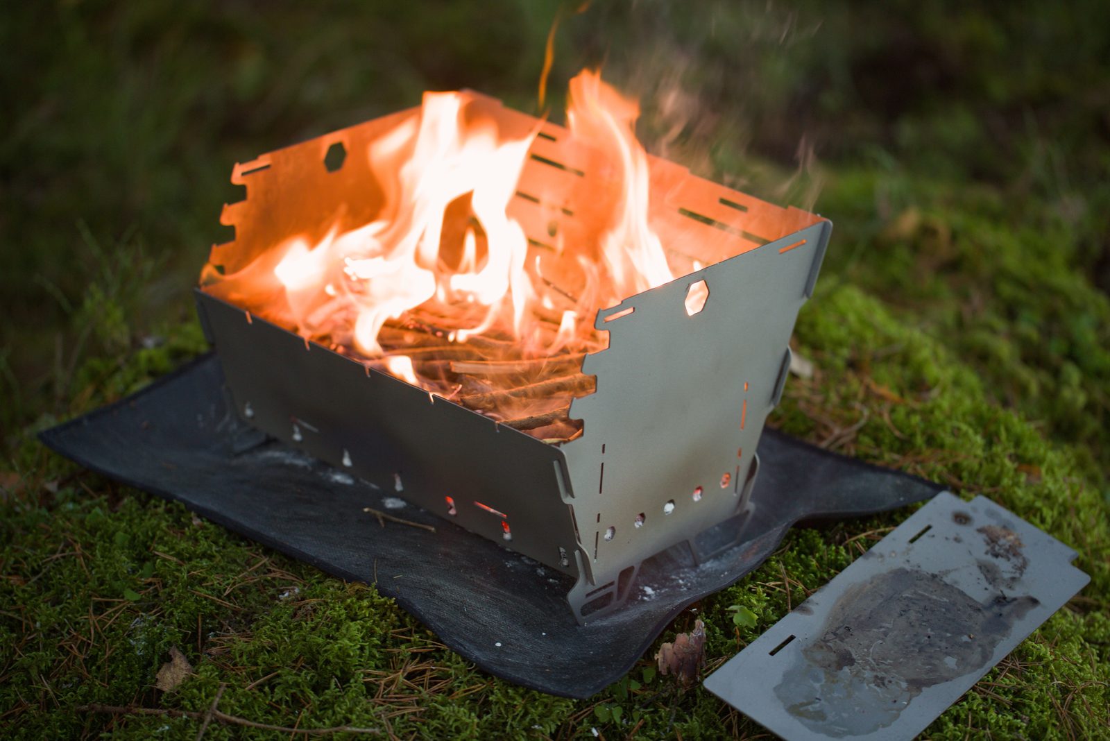 Titan1 burning with a tall flame on its base mat, plancha plate resting alongside
