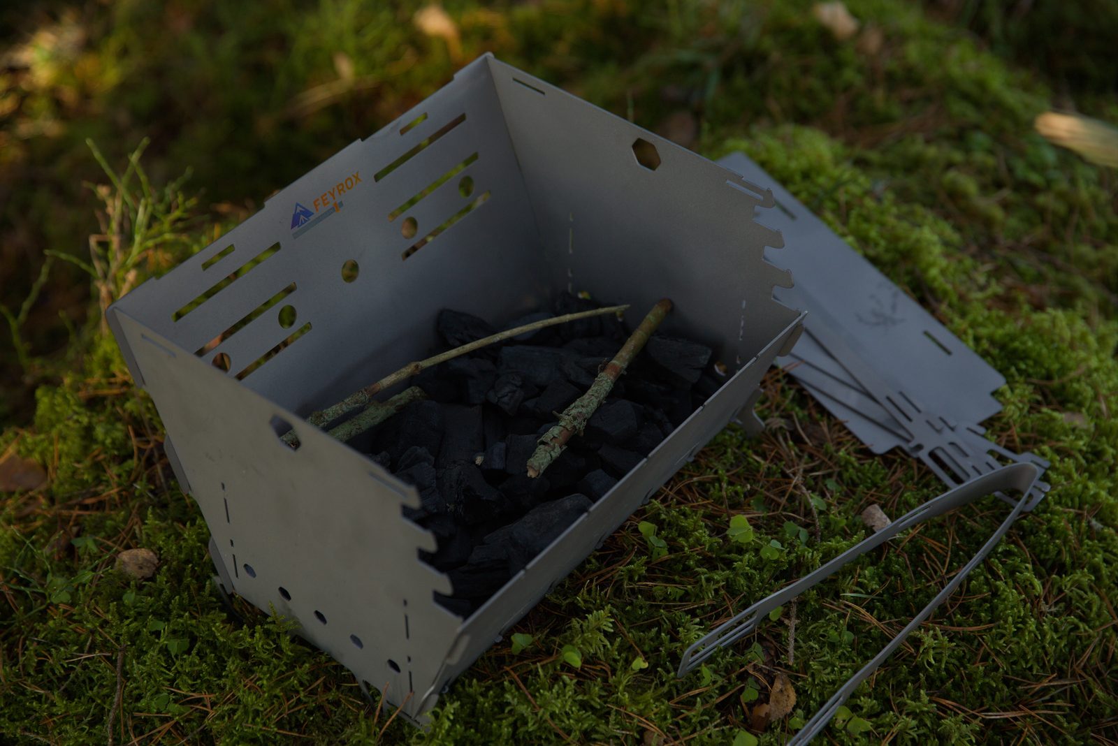 Titan1 opened out and loaded with charcoal, folded panels laid beside it on moss